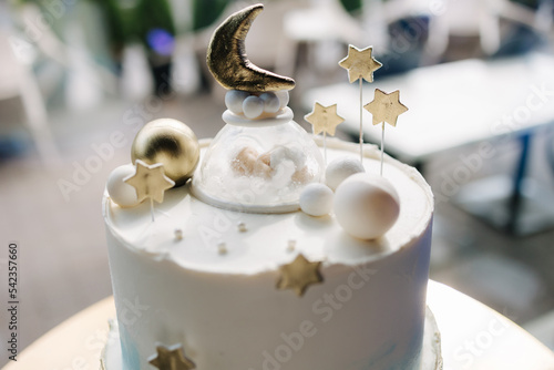 Close-up of beautiful cake for Christening. White cake decorated by stars from sugar. Gold stand