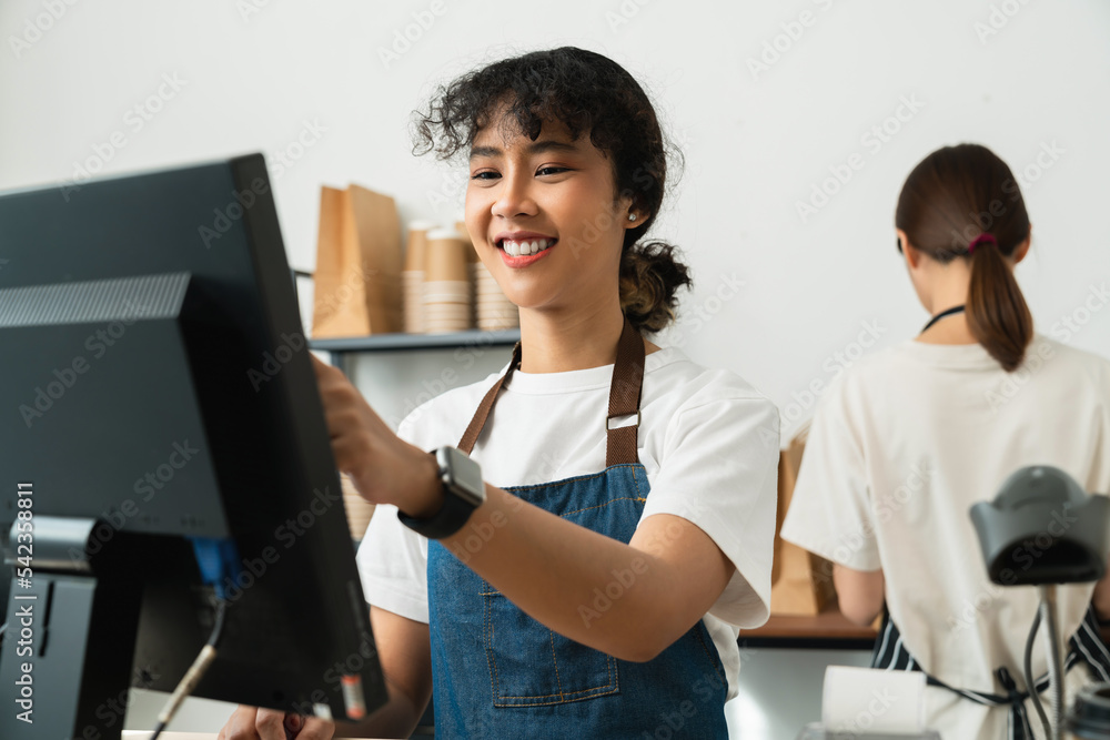Happy young Asian woman cashier wears an apron and using pos terminal to input orders on coffee shop counter. Happy young Asian woman cashier wears an apron and using pos terminal to input orders on coffee shop counter.