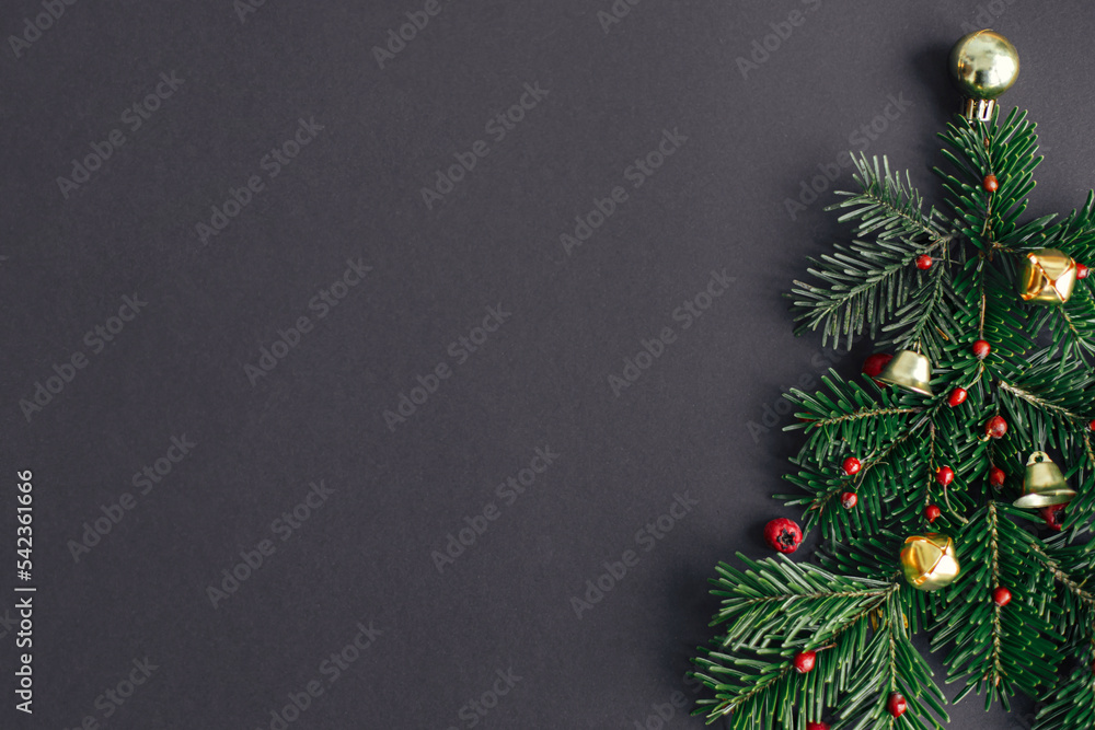 Stylish christmas tree made of fir branches, red berries and gold baubles on black background. Creative christmas idea, winter holidays. Merry Christmas! Modern festive flat lay, space for text