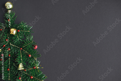 Stylish christmas tree made of fir branches, red berries and gold baubles on black background. Creative christmas idea, winter holidays. Merry Christmas! Modern festive flat lay, space for text