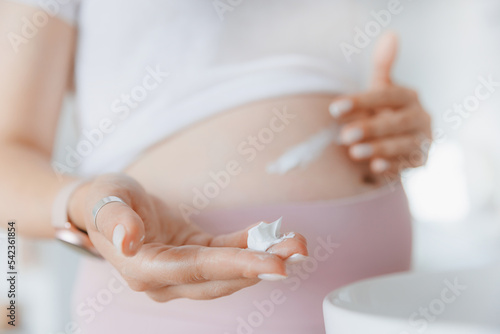 Closeup cream in hand of pregnant woman for belly to moisturize skin and improve elasticity to prevent stretch marks. Concept care health pregnancy