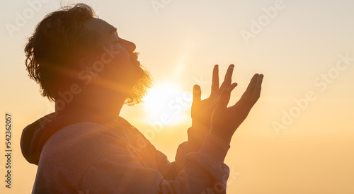 Portrait of young adult male with beard praying for thank god golden sunset sky background.