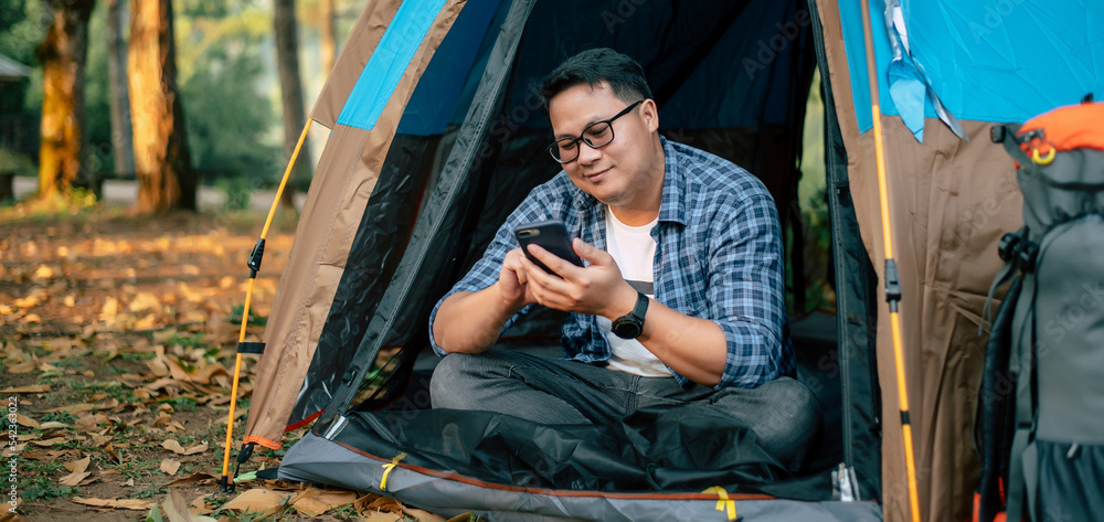 Portrait of Asian traveler man glasses using smartphone in tent camping Portrait of Asian traveler man glasses using smartphone in tent camping