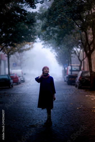 Obraz na płótnie A woman in a blue coat on a street in a dense fog. w salonie
