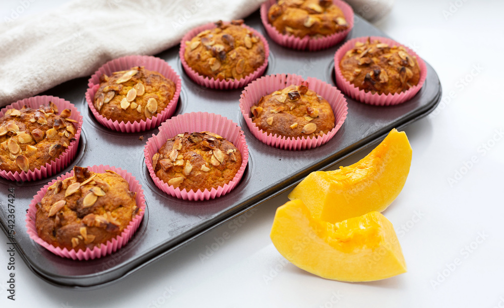 Homemade pumpkin muffins with pumpkin seeds and walnut pieces. Fall baking for Thanksgiving and Halloween. Cupcakes in baking dish on linen napkin. Selective focus. Close up.