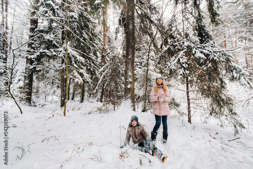 A happy boy is sitting in the snow next to a girl in the forest