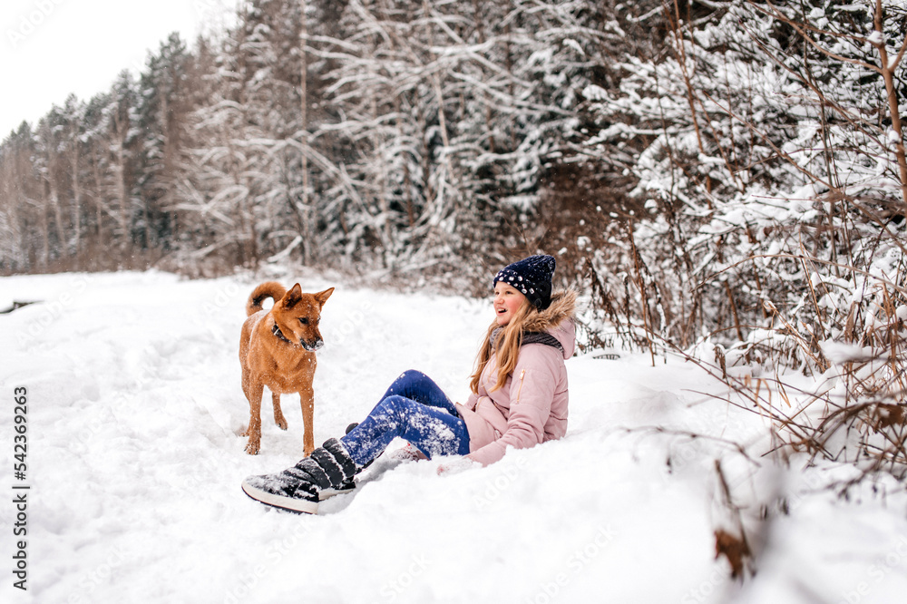 A cute girl is sitting in the snow next to a dog