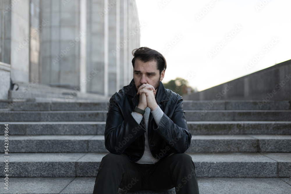 saddened and men sits in depression on the steps of a gray building saddened and men sits in depression on the steps of a gray building