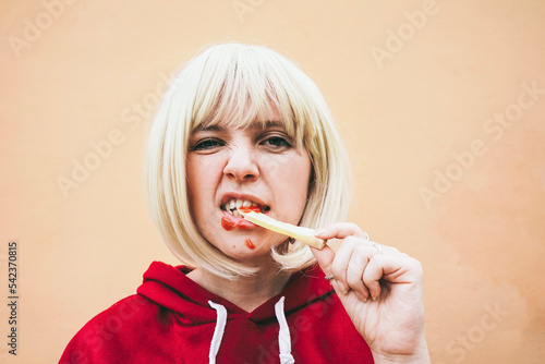 Woman eating French fries with ketchup in front of peach wall photo