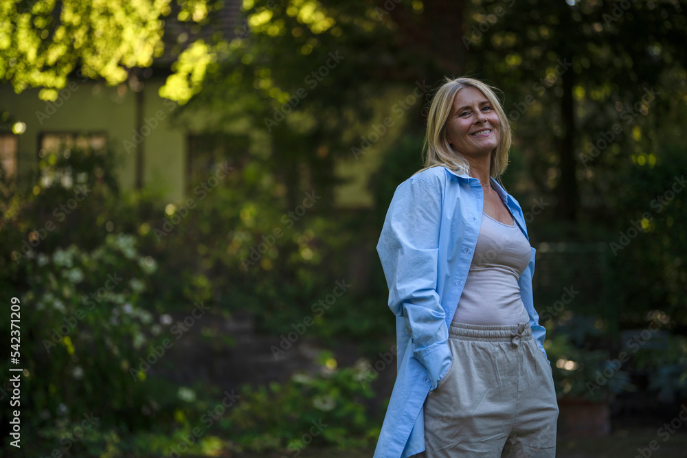 Happy mature woman standing with hands in pockets at garden Happy mature woman standing with hands in pockets at garden
