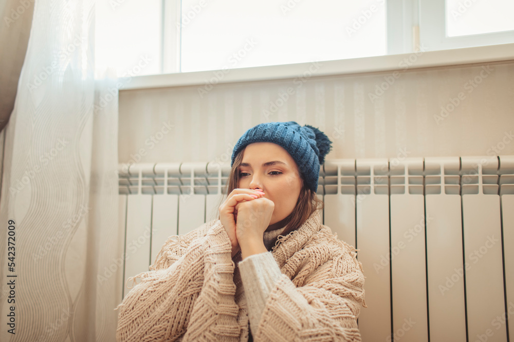 Woman wearing knit hat wrapped in blanket leaning on radiator Woman wearing knit hat wrapped in blanket leaning on radiator