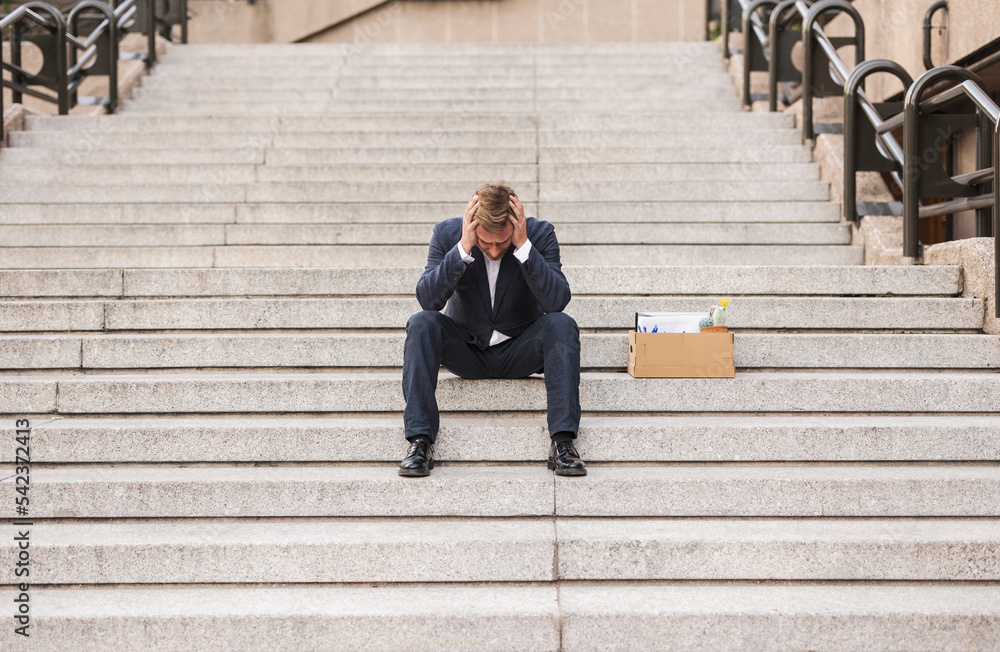Worried businessman sitting with cardboard box on stairs Worried businessman sitting with cardboard box on stairs