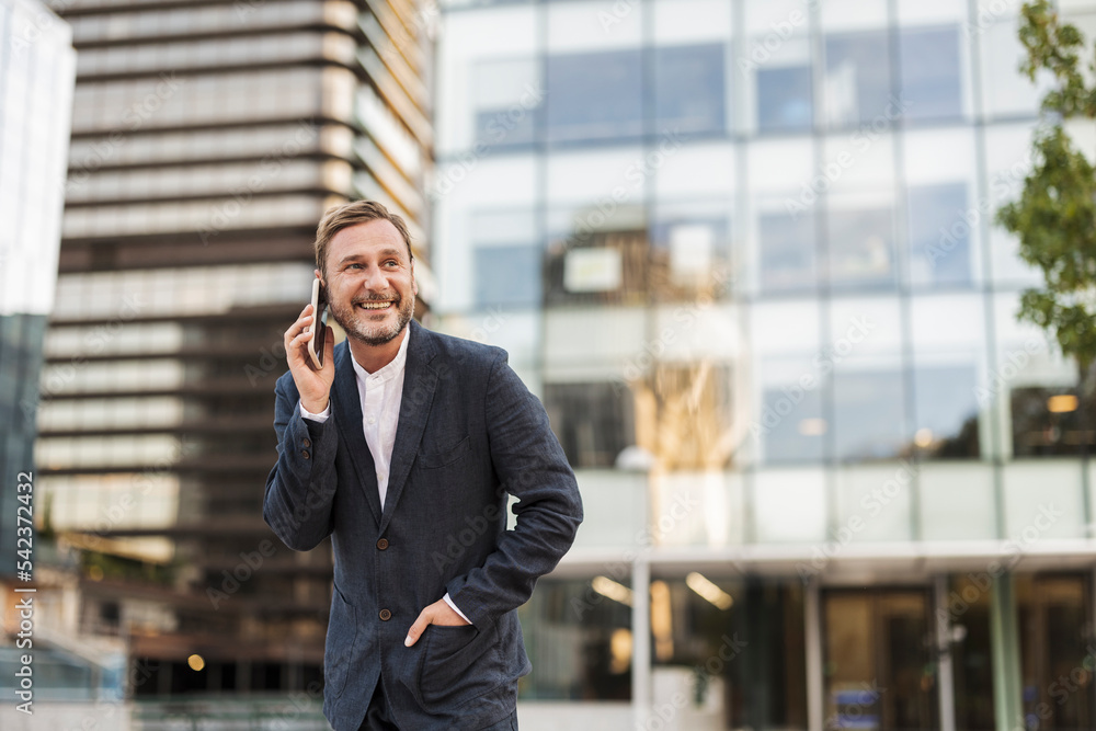 Smiling businessman talking over mobile phone in front of building Smiling businessman talking over mobile phone in front of building
