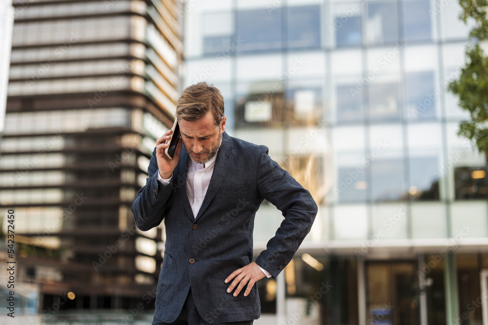 Tensed businessman talking on smart phone in front of office building Tensed businessman talking on smart phone in front of office building