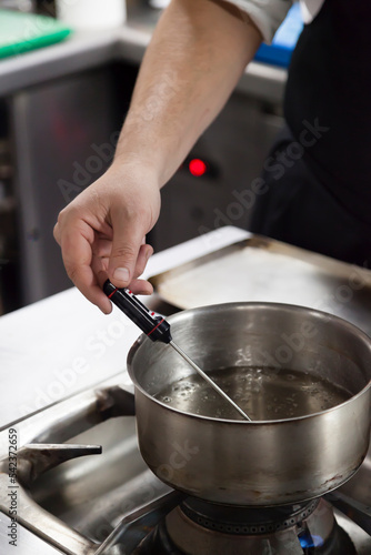 Chef hand using thermometer on boiling water vertical stills.