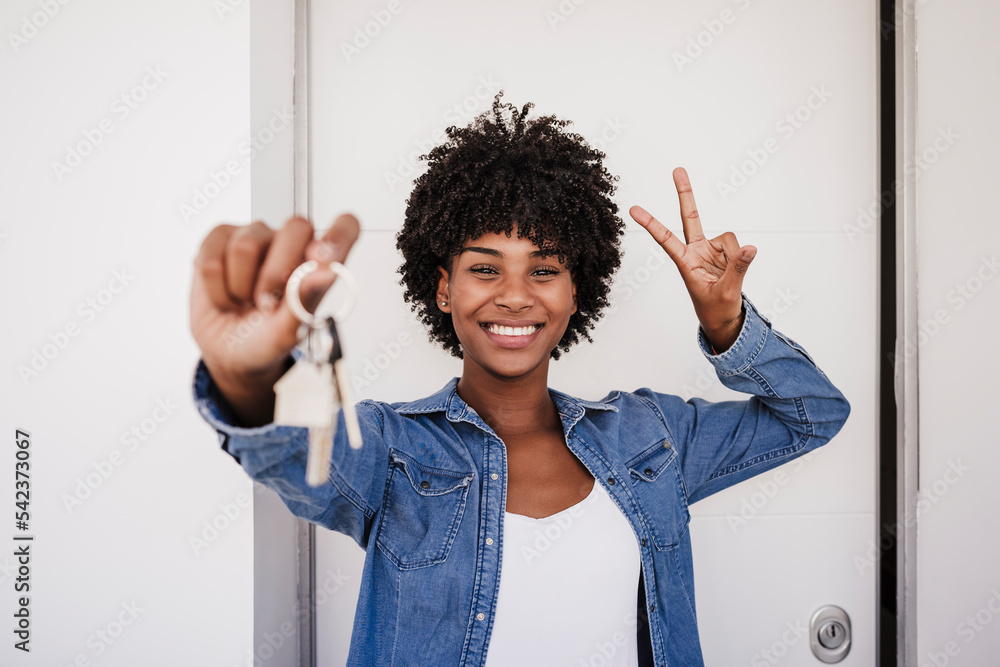 Happy woman showing house keys and peace sign gesture in front of door ...