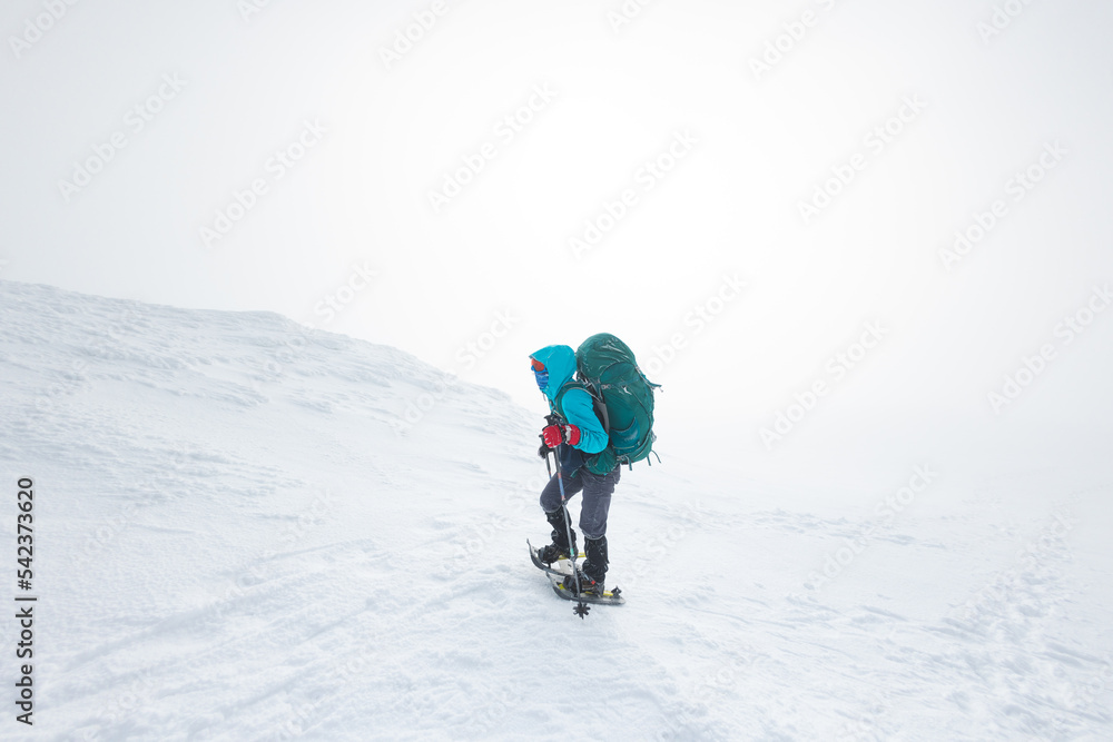 girl with a backpack and snowshoes walks through the snow during a snow storm.