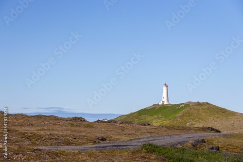 Lighthouse atop a green hill in Iceland under a clear pale blue sky on a sunny day