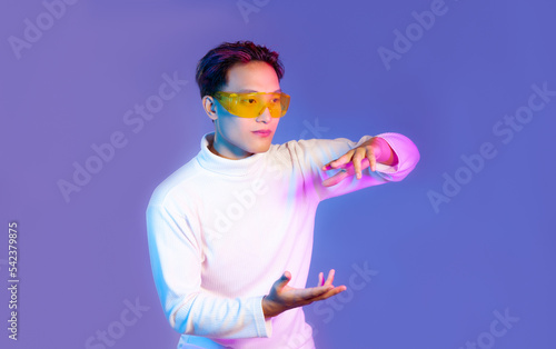 Metaverse concept, asian man wearing vr goggles watching playing and touching blue color background. 