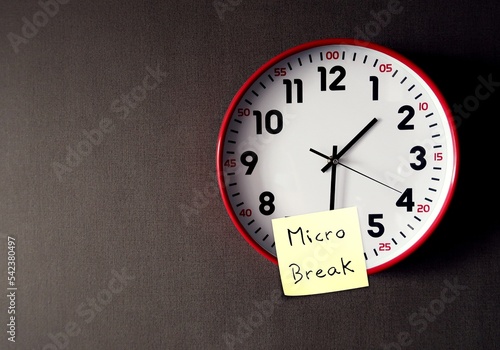 On copy space gray wallpaper, clock with stick note written MICRO BREAK, to break up from tasks or static postures by taking short tiny break to improve well being, keeping mind fresh and energized photo