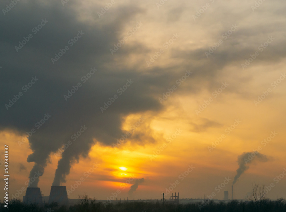 Industrial landscape in Russia. Smoke from Cogeneration rises very high against an orange evening sky at sunset Industrial landscape in Russia. Smoke from Cogeneration rises very high against an orange evening sky at sunset