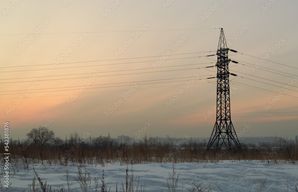 Power line stands in a winter field with dry grass against the background of the evening sky at sunset
