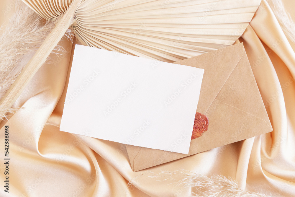 Blank card and envelope on beige satin fabric and dried palm leaf close up, romantic mockup Blank card and envelope on beige satin fabric and dried palm leaf close up, romantic mockup