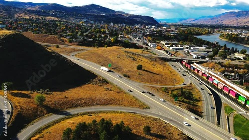 dolly in drone shot hyperlapse of Kamloops BC Canada with Bridges, the Highway 1 and Yellowhead Highway 5 on a sunny day in the desert city with cars,semi trucks and trains driving in the foreground photo