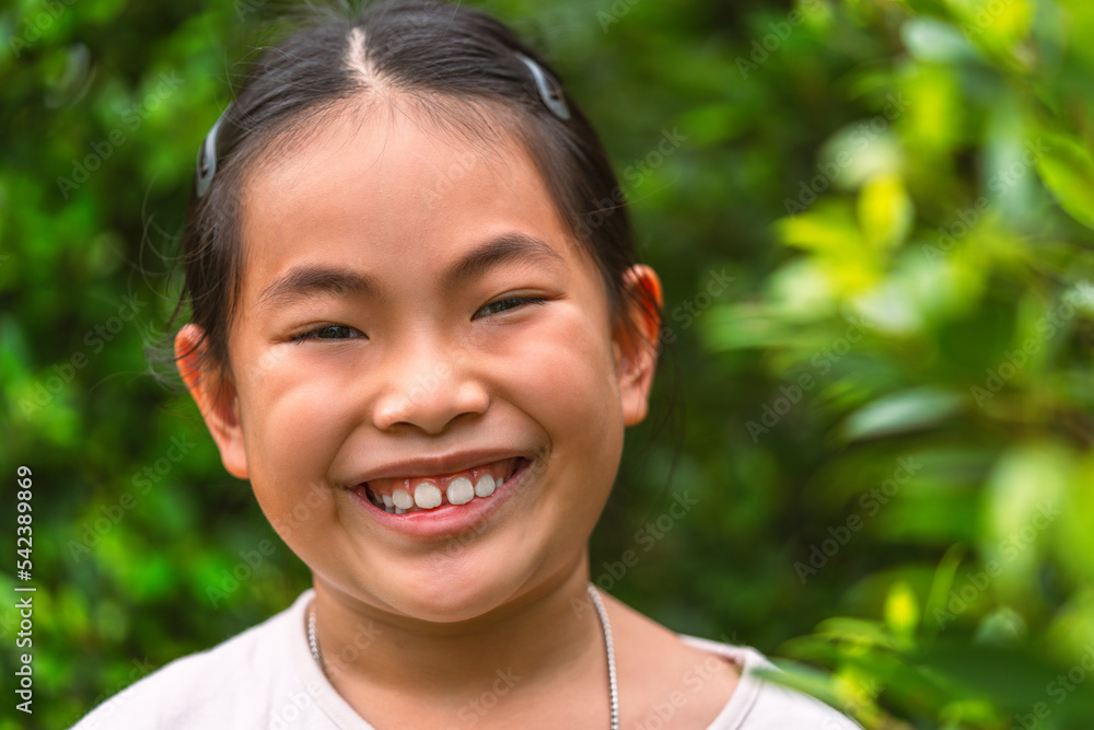 Portrait healthy Asian child girl with a big smile, standing outdoors in a park, with blurred background of the green bush, headshot of a cute little girl, space for text. Portrait healthy Asian child girl with a big smile, standing outdoors in a park, with blurred background of the green bush, headshot of a cute little girl, space for text.