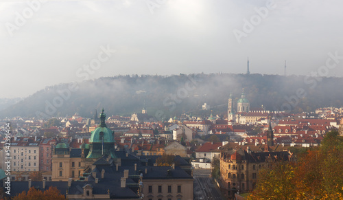 Old Town of Prague with dissolving morning fog with Petrin hill, St. Nicholas Cathedral and rooftops of Lesser Quarter.