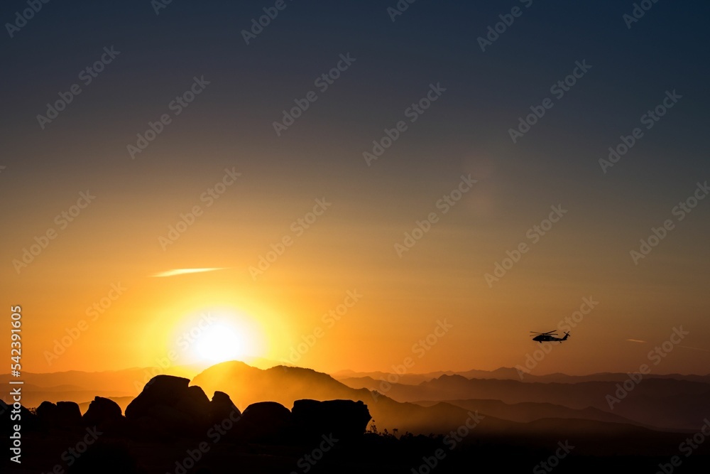 Helicopter flying between mountains during orange sunset