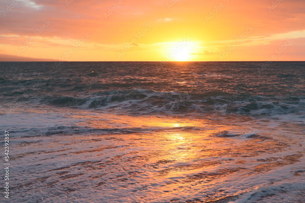 Sunset over a stormy sea. The orange sun on the horizon reflects on the surface of the water