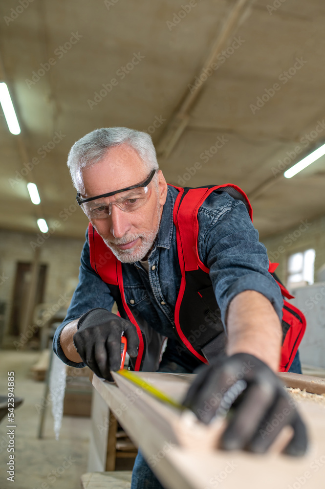 Gray-haired carpenter making measurements and looking involved