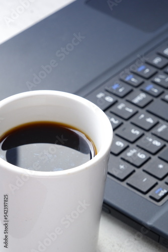 コーヒーを飲みながらノートパソコン（黒）でデスクワーク