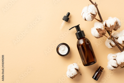 Natural cosmetics concept. Top view photo of amber pump bottle without label dropper bottle cream jar and cotton branch on isolated beige background with blank space