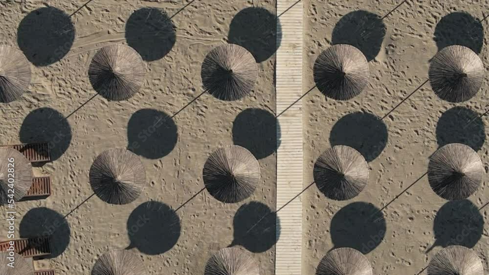 Woven beach parasols and boardwalk on hot sand form repeating pattern Woven beach parasols and boardwalk on hot sand form repeating pattern