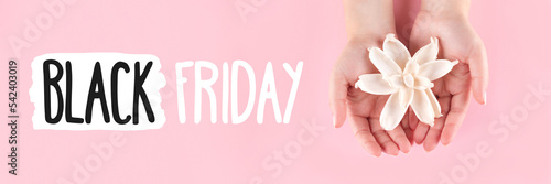 Black Friday sign on pink background banner with female hands with beautiful manicure - pink nude nails with white dried flower, wide panoramic header. Shopping concept