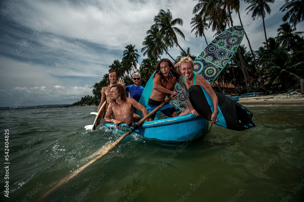Obraz premium Group of surfers ride on vietnam wooden boat to surf session on coastal vilage
