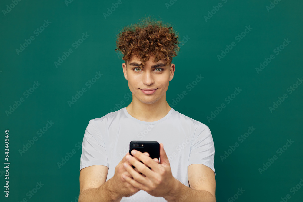 a funny, joyful man with curly hair stands against a green background and holds his smartphone with both hands, smiling pleasantly and looking at the camera a funny, joyful man with curly hair stands against a green background and holds his smartphone with both hands, smiling pleasantly and looking at the camera