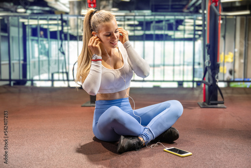 Young sporty woman listening to music in gym. Attractive blonde woman taking a break in a gym.