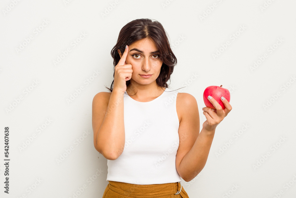 Young Indian woman holding an apple isolated on white background pointing temple with finger, thinking, focused on a task. Young Indian woman holding an apple isolated on white background pointing temple with finger, thinking, focused on a task.