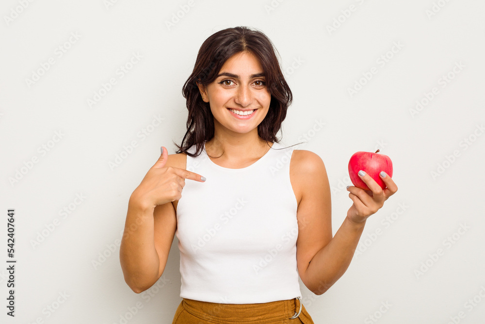Young Indian woman holding an apple isolated on white background person pointing by hand to a shirt copy space, proud and confident Young Indian woman holding an apple isolated on white background person pointing by hand to a shirt copy space, proud and confident
