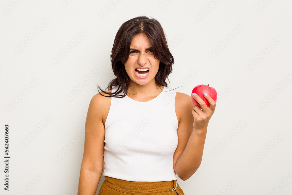 Young Indian woman holding an apple isolated on white background screaming very angry and aggressive. Young Indian woman holding an apple isolated on white background screaming very angry and aggressive.