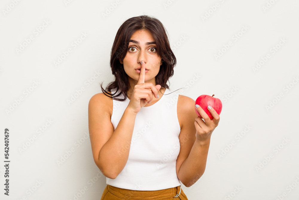 Young Indian woman holding an apple isolated on white background keeping a secret or asking for silence. Young Indian woman holding an apple isolated on white background keeping a secret or asking for silence.