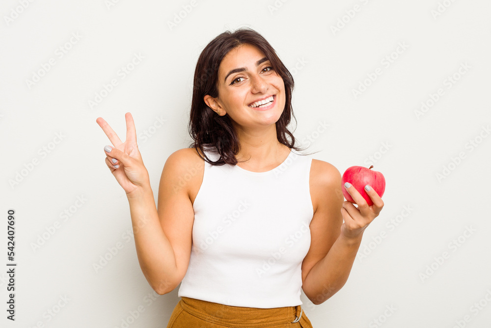 Young Indian woman holding an apple isolated on white background joyful and carefree showing a peace symbol with fingers. Young Indian woman holding an apple isolated on white background joyful and carefree showing a peace symbol with fingers.