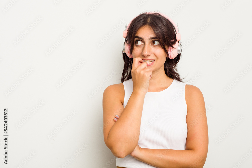 Young Indian woman wearing headphones isolated on white background relaxed thinking about something looking at a copy space. Young Indian woman wearing headphones isolated on white background relaxed thinking about something looking at a copy space.