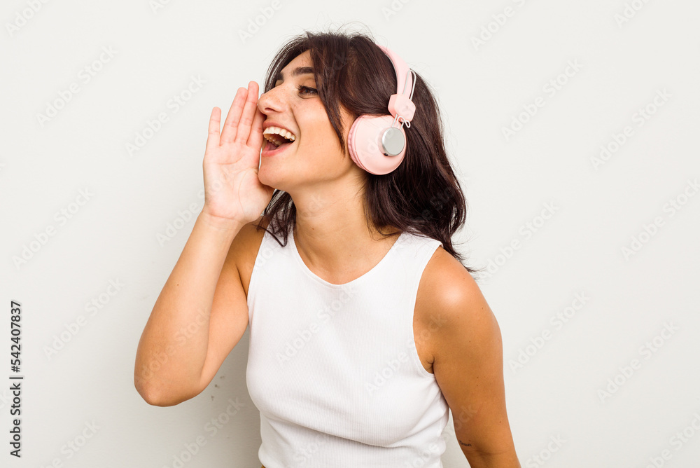 Young Indian woman wearing headphones isolated on white background shouting and holding palm near opened mouth. Young Indian woman wearing headphones isolated on white background shouting and holding palm near opened mouth.