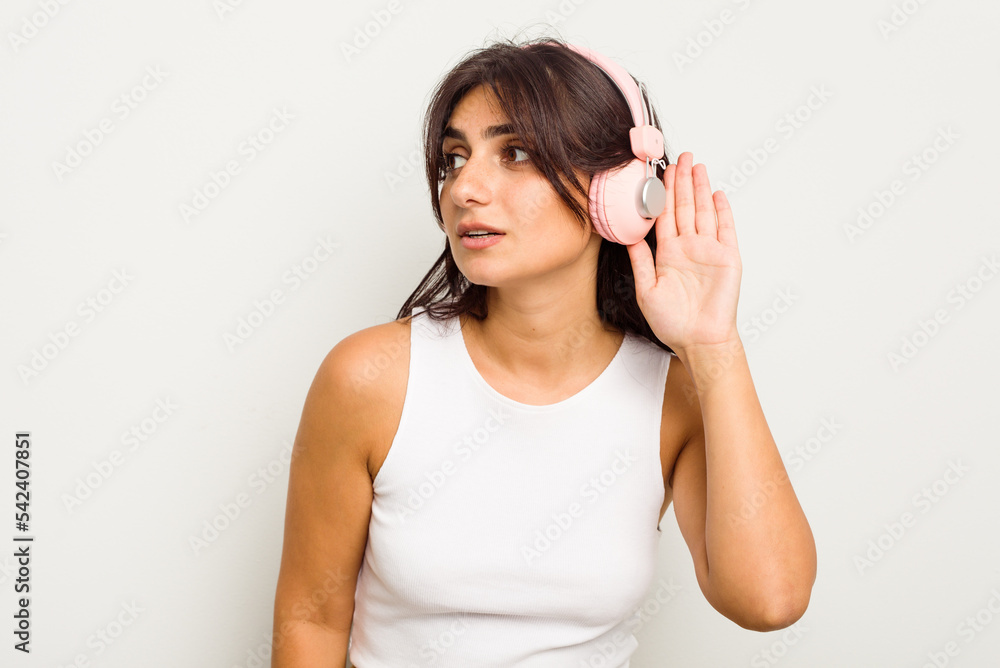 Young Indian woman wearing headphones isolated on white background trying to listening a gossip. Young Indian woman wearing headphones isolated on white background trying to listening a gossip.