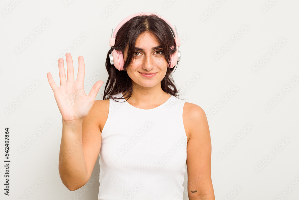 Young Indian woman wearing headphones isolated on white background smiling cheerful showing number five with fingers. Young Indian woman wearing headphones isolated on white background smiling cheerful showing number five with fingers.