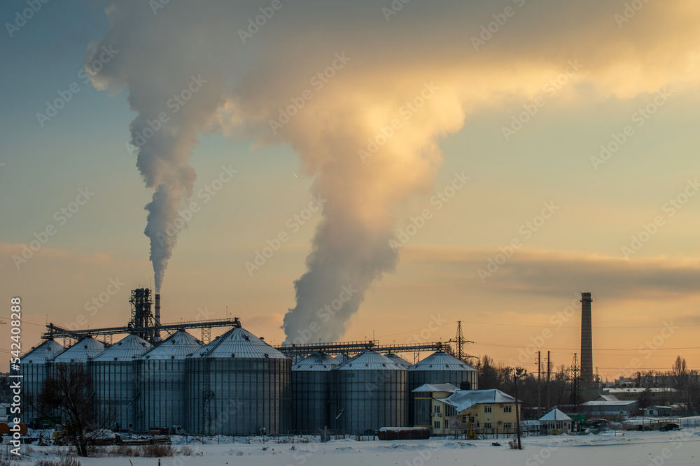 Elevator for grain storage against the background of smoking chimneys. Evening winter photo.